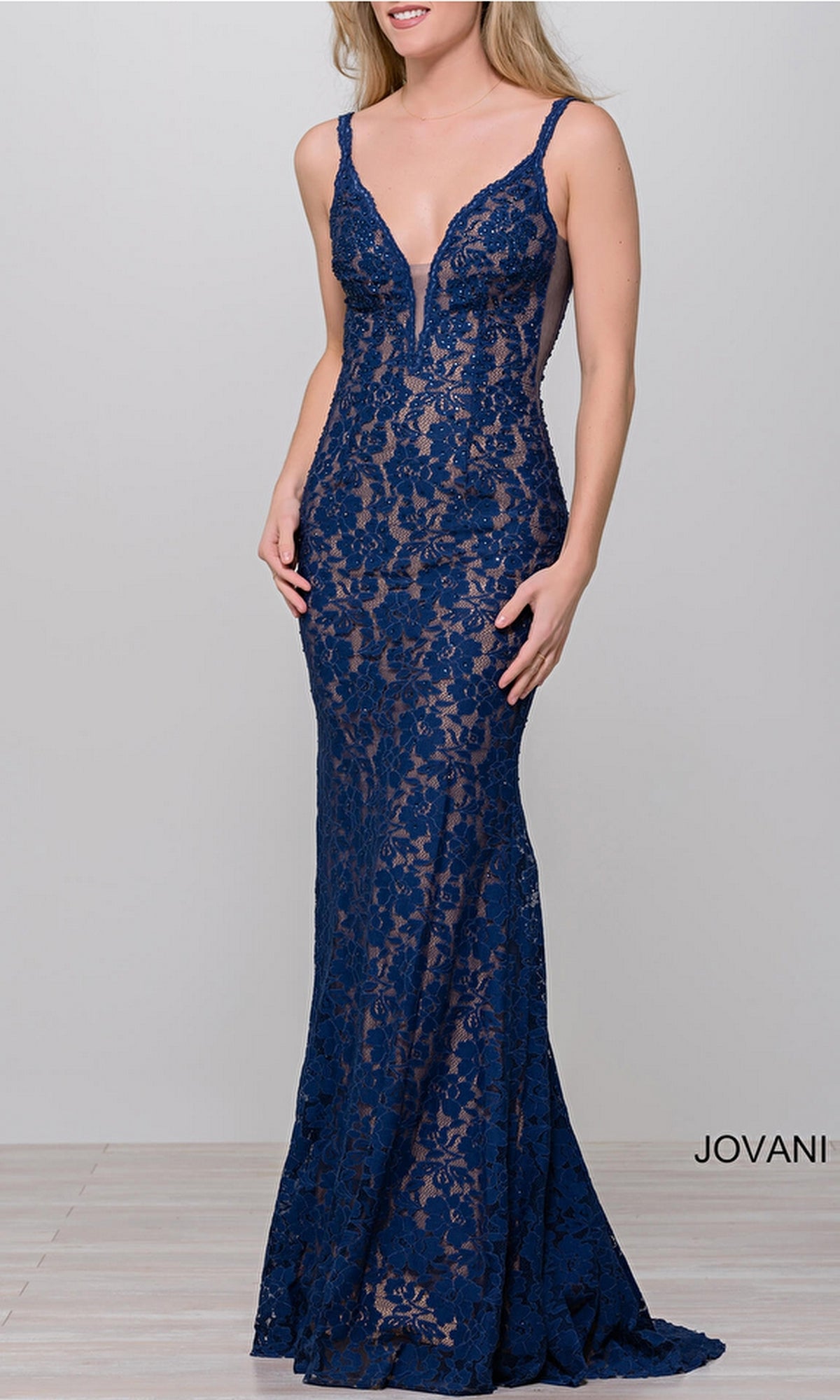 A woman models the Jovani 48994 Illusion-Sides Long Lace Prom Dress, featuring a sleeveless, deep V-neck, fitted silhouette, open back, and lace details against a plain light background.
